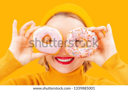 Portrait of funny woman with colorful donuts against her eyes on yellow background