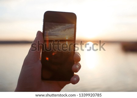 Male hand holding smartphone and taking the photo of sunset.