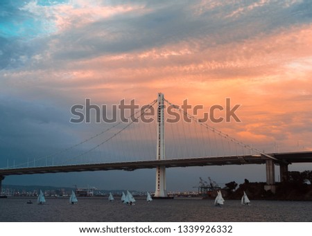 Bay Bridge at sunset with sailboats under it.