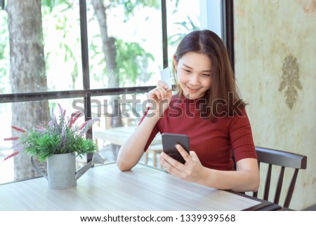Happy young girl holding credit card while using mobile phone select shopping online