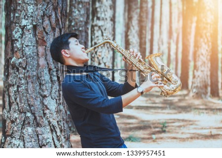 A man holding and plays saxophone at pine trees forest, outdoor activity, music background with copy space