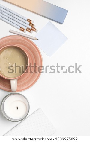 Home office workspace with cup of coffee with cream, light blue stationery and candle on white background. Top view, flat lay.