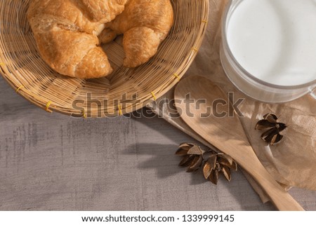 Top view of croissant in the basket, a cup of milk, wooden spoon on the table with copy space. Soft  breakfast