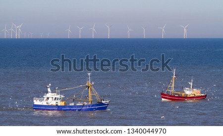 a blue and a red cutter with a flock of seagulls on the North Sea in the sun with wind generators in the background