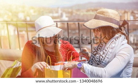 Couple of young women on a rooftop looking inside gift bags.