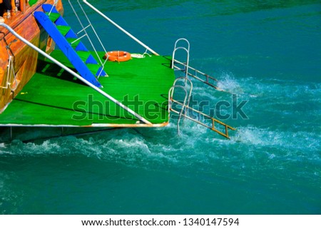 The back of the pleasure yacht with a green cover and a ladder for descent into the water. Photos of the ship from the sea. The concept of summer recreation, sport, tourism