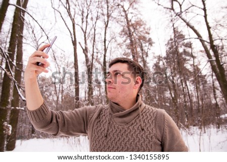 man in a sweater in the winter in the woods. man in the winter forest makes a photo on the phone. 