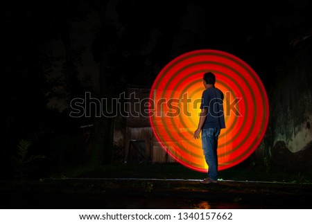 one person standing in front the light of a red  circle with a dark background