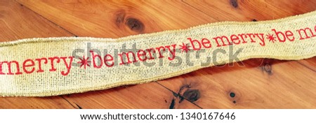Be Merry at Christmas festive saying on a hessian ribbon sitting on a wooden table