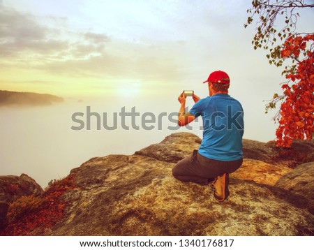 Man taking picture of amazing fall mountains on his phone in misty weather
