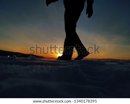 silhouette the legs that are walking on the ice floor on the lake baikal with sunset. the dark shape and outline of people visible against a lighter background in dim light.