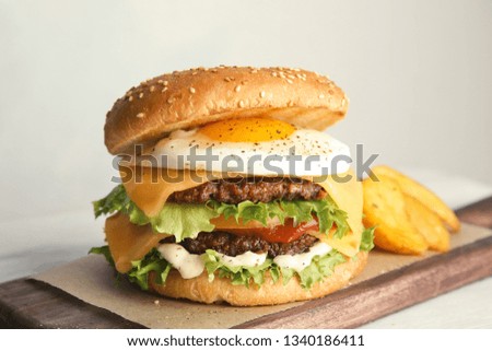 Tasty burger with fried egg on board against light background