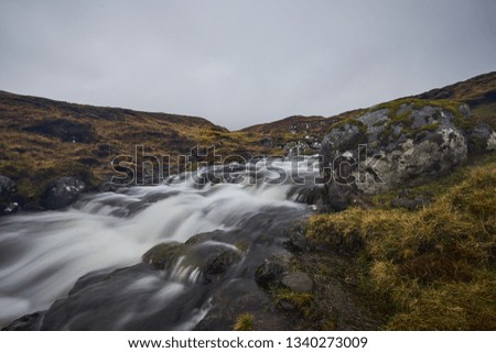 Wild stream or creek in moorland or heath in the highland of Faroe island Vagar with waterfall cascades and stones with moss and lichen on them. Picture taken in cloudy, misty, foggy and rainy day.  