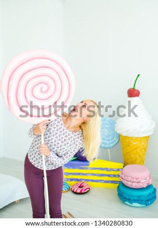 Amusing blonde girl express surprise on decorated background with sweets. Amazing sweet-tooth woman surrounded by toy sweets and ice cream.