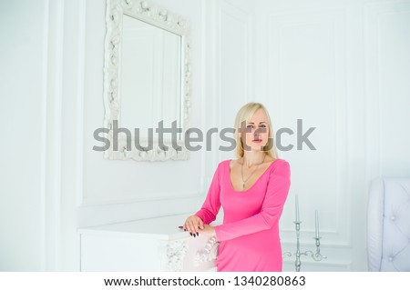 Beautiful blonde girl standing near big mirror in white room. Horizontal portrait