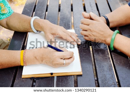 Elderly's female hand writing in white notebook, learning on dark brown plank wooden table in the park, crop picture in vintage tone with shadow light of sunny, never too late for learn concept