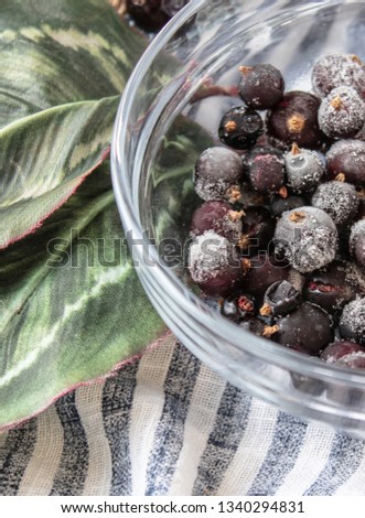 Berries of frozen currants in a glass bowl. Ice on the berries. Dark berries in the ice.