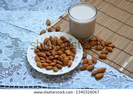 Almonds in a white plate with a glass of almonds milk. 