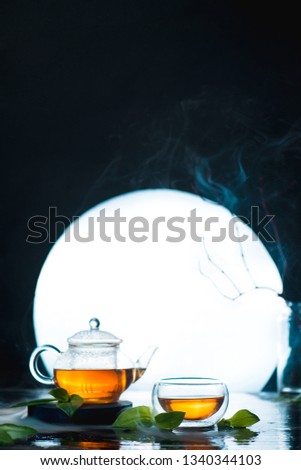 Asian tea ceremony with a full moon. Glass tea bowl and teapot against a shining circle. High contrast drink photo
