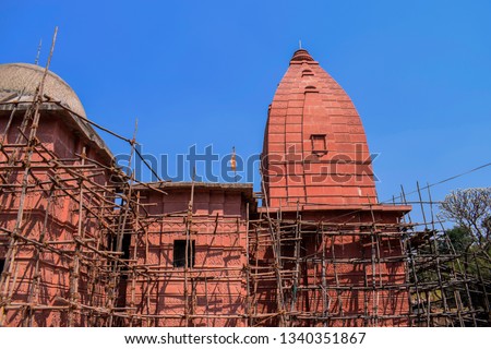 Stock photo of architectural and renovation site of old hindu temple,bamboo scaffolding on red color painted temple building . Picture captured under bright sunlight at Naikba Mandir patan, satara.