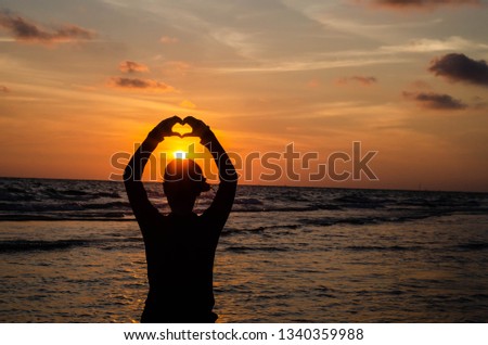 The silhouette of a woman who raised his hand to create a heart shape in the sea at sunset The idea may be a background or wallpaper.