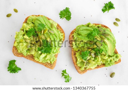 Avocado toasts with pumpkin and chia seeds on whole grain bread. Top view on a bright marble background.