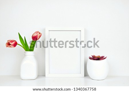 Mock up white frame with succulent plant and tulip flowers on a shelf or desk. White shelf and wall. Portrait frame orientation.