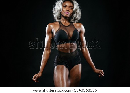 Sporty beautiful afro-american bodybuilder model, woman in sportwear makes fitness exercising at black background to stay fit