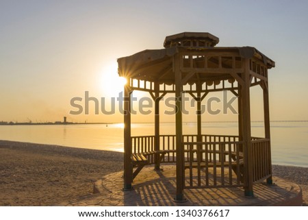 Wooden gazebo on the empty beach with sunburst in the background during sunset located in Kuwait.