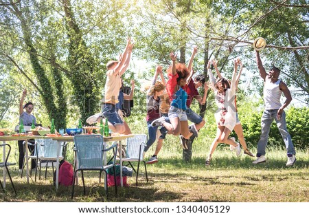 Multiracial friends jumping at barbecue pic nic garden party - Friendship multicultural concept with young happy people having fun dancing out at spring break camp festiva - Bright warm filter