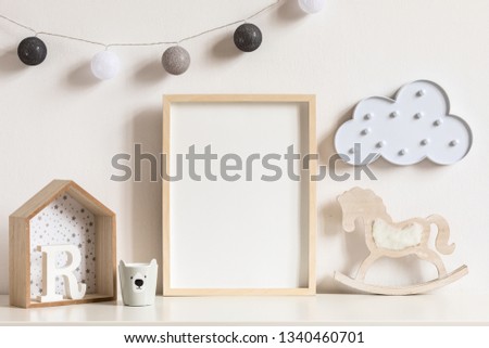 The modern scandinavian newborn baby room with mock up photo frame, wooden toys and children's cup. Hanging cotton lamps and white cloud. Minimalistic and cozy interior with white walls. Real photo.