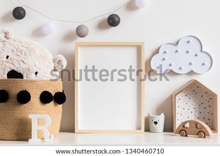 Stylish and modern scandinavian newborn baby interior with mock up photo or poster frame on the white shelf. Wooden toys, teddy bear, cup and hanging cotton lamps and star. Template. Blank. Real photo