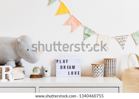 The modern scandinavian newborn baby room with plush rhino, design boxes, mock up blackboard andnatural basket. Hanging cotton flags on the white background wall. Stylish and cozy interior.