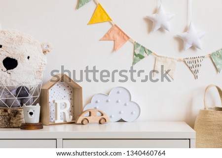 Stylish scandinavian nursery interior with  white teddy bear, wooden toys and star. Hanging cotton flags and natural basket on the white background wall. Cozy and sunny childroom.