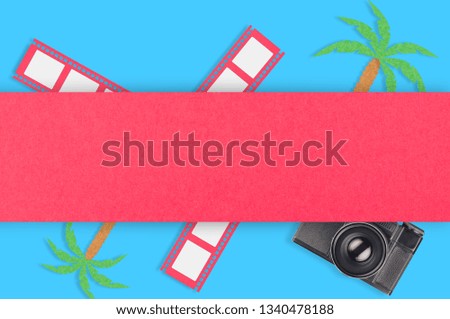 Old vintage camera for photo near palm trees and film strip cut out of colored paper under red line on blue table. Top view. Travel concept. Copy space for your text