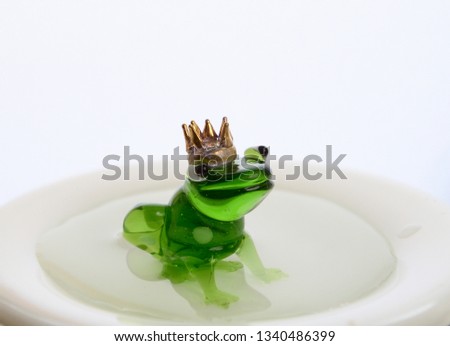 Green Glass Frog with Crown sitting in pool of water.
