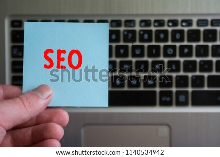 red word SEO on sticky note hold in hand on laptop keyboard background.