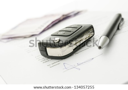 Black car key and money on a signed contract of car sale.  Focus on a key.