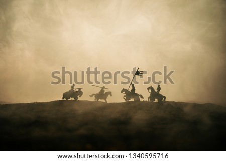 Medieval battle scene with cavalry and infantry. Silhouettes of figures as separate objects, fight between warriors on sunset foggy background. Selective focus Royalty-Free Stock Photo #1340595716