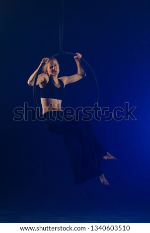 gymnast girl aerial acrobatics on the ring on the background of blue smoke in the dark