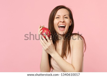 Cheerful young woman in light clothes holding fresh ripe pitahaya, dragon fruit isolated on pink pastel wall background in studio. People vivid lifestyle, relax vacation concept. Mock up copy space