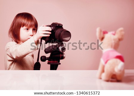 Little cute child girl photographer takes portrait of toy dog with a DSLR camera. Selective focus on eye.