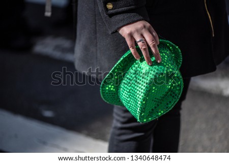 Woman in black coat holding green St. Patrick Day hat