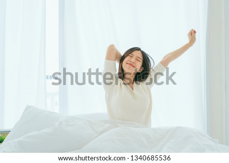 white dress asian beautiful woman stretching morning wake up bedroom with white curtain background lifestyle home concept Royalty-Free Stock Photo #1340685536