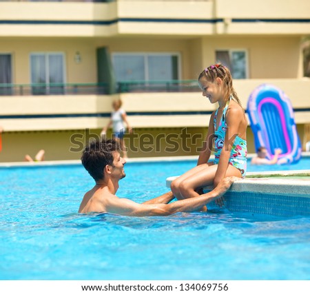 Cute girl with her father playing in a pool of water during the summer