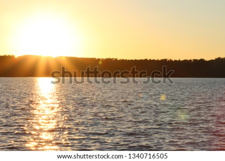Sunset over a lake with lens flare and ray cast on the lake and treeline in silhouette in the background during summer and a sunburst