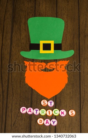 Paper Saint Patrick's day leprechaun props: green leprechaun hat and orange beard with mustache as symbol of Ireland traditional holiday on wooden background
