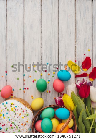 Colorful easter eggs, cake, spring tulips  on wooden texture background. On a white wood table, colored eggs, flowers, bread. Happy religious day, traditional for people. Top view. Copy space.