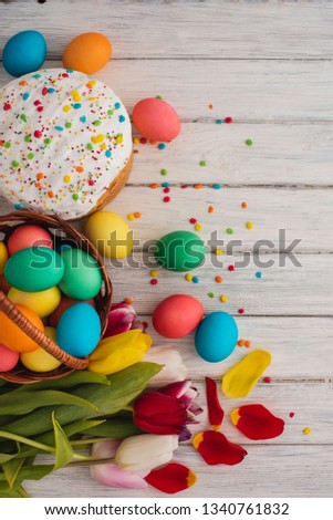 Colorful easter eggs, cake, spring tulips  on wooden texture background. On a white wood table, colored eggs, flowers, bread. Happy religious day, traditional for people. Top view. Copy space.