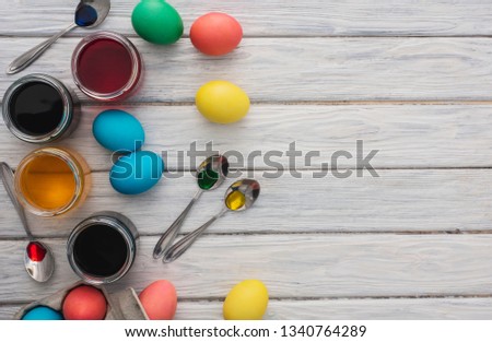 Colorful easter eggs on wooden background. On a white wood table colored eggs, paint, spoons.Happy religious day, traditional for people. Top view. Copy space.
